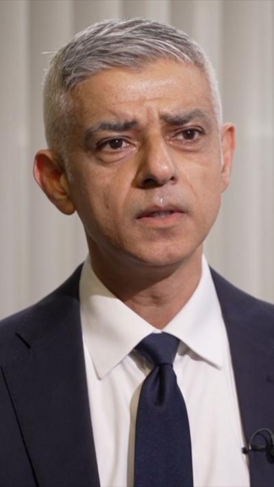 Khan speaking during interview, wearing a suit and tie and worried expression.