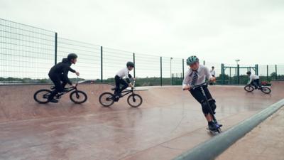 Four students ride their bikes and scooter on a purpose built skate park in their school yard.