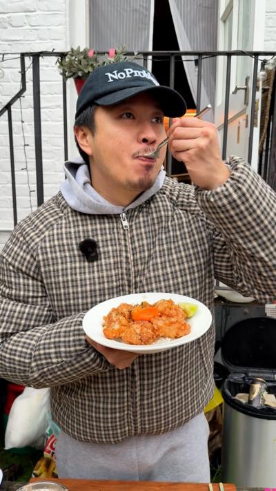 A man in a checked top and baseball cap eats from a spoon while holding a bowl of food