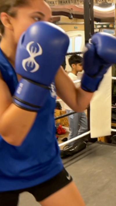 A young woman with blue boxing gloves in a ring with a blue vest