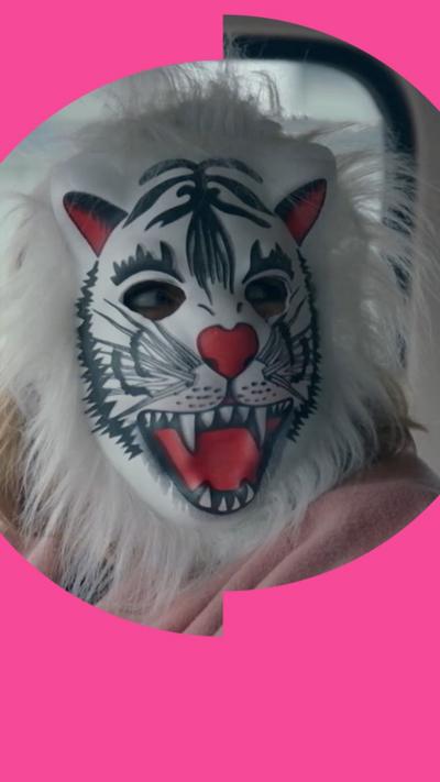 A woman wears a white tiger mask inside a van