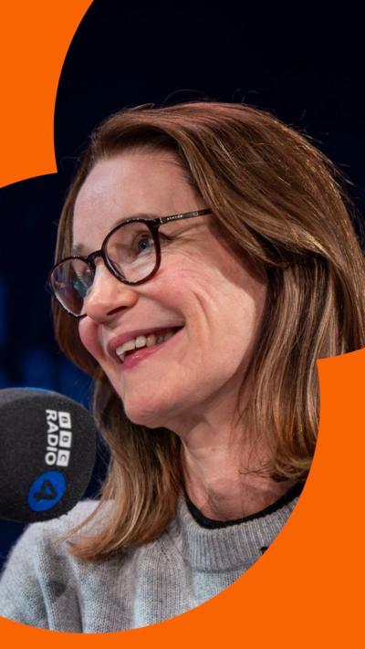 Susie Dent is wearing a grey jumper in front of a black Radio 4 microphone