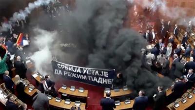 Smoke filling the Serbian parliament's chamber as MPs hold up a black banner.