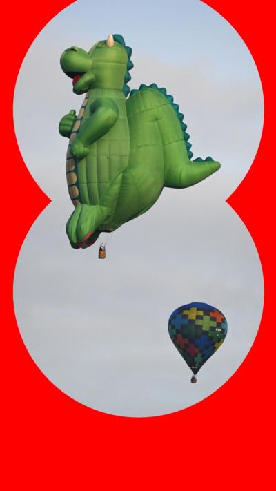 A hot air balloon shaped like a green dragon flies in the sky