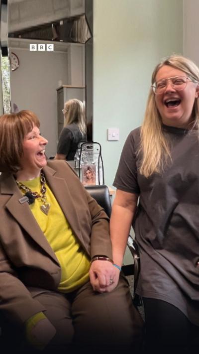 Two women sitting beside each other laughing.