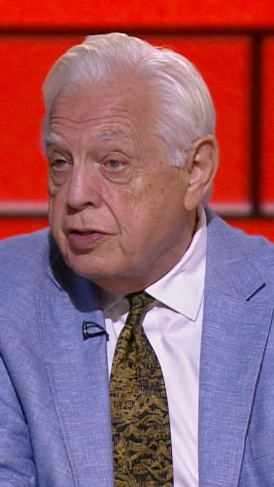 John Simpson in a blue suit and black and gold tie