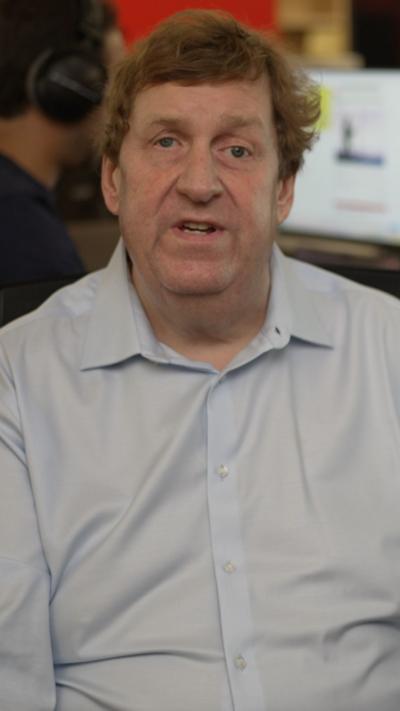 BBC's Gary O'Donoghue speaks towards a camera from inside a newsroom, where a man in headphones sits in the background.
