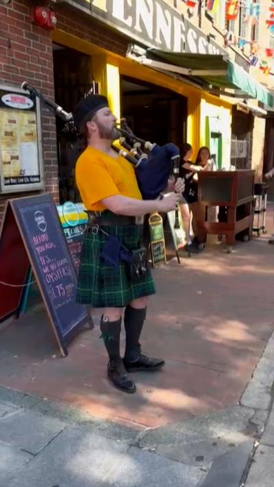 Piper wearing a kilt plays bagpipes outside a pub in Boston
