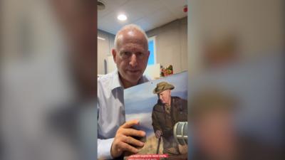 Steve Rosenberg holds a calendar featuring an image of Vladimir Putin wearing a green hat and brown jacket