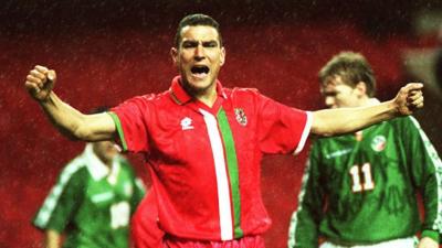Vinnie Jones with arms out wide and shouting in Wales kit