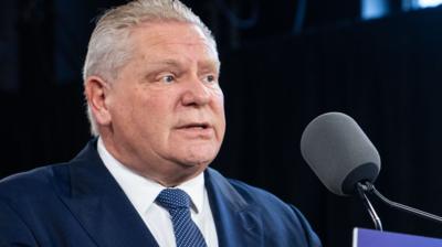 Doug Ford speaks into a microphone wearing a blue suit, white shirt and blue tie.