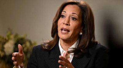 Former Vice President and 2024 Presidential nominee Kamala Harris gesturing with her hands and talking. She is sitting down wearing a black pinstripe jacket and being interviewed