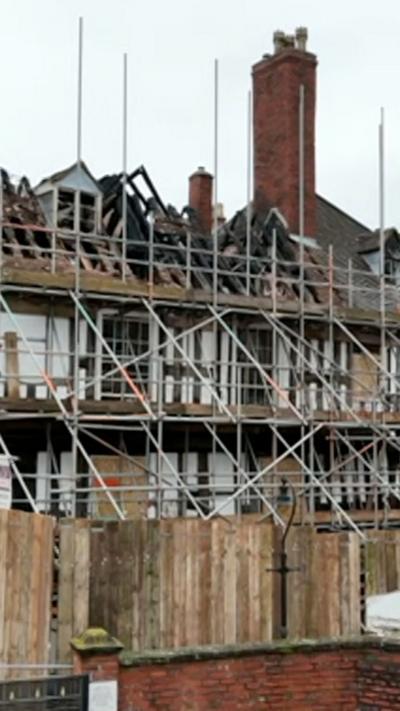 A fire damaged black and white house encased in scaffolding