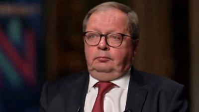 Andrei Kelin in a red tie sits in a dark room