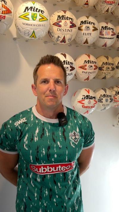 Simon Francis is stood at the top of his stairs wearing a green with black and white stripes and smiling straight at the camera. 