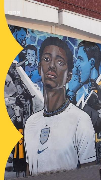 A street art painting of Jude Bellingham, wearing an England shirt, with other footballers painted in blue surrounding him on a Stourbridge wall