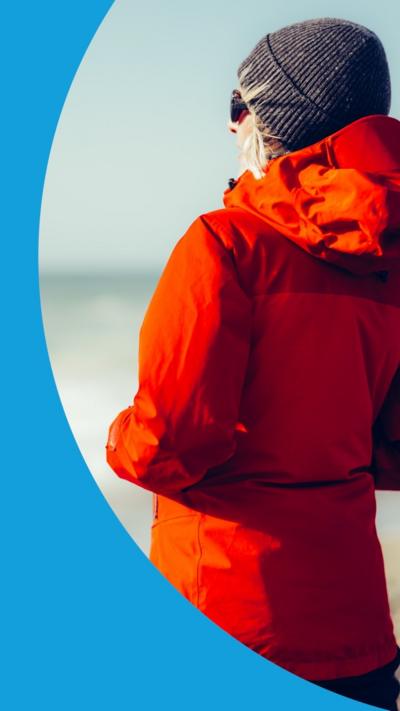 Back of a person wearing a red rain jacket looking out at sea from a beach