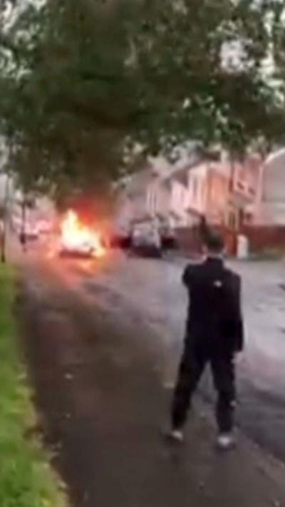 Grainy footage of a car being pushed down a hill on fire
