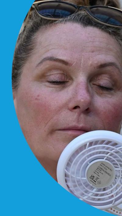 A woman holds a small fan up to her face
