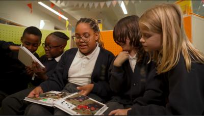 Five primary school children sit on benches at look at scrap books on their laps