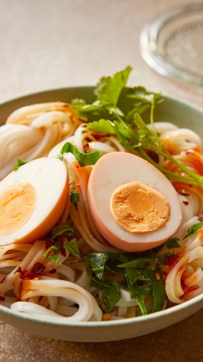 A green bowl with pickled eggs sitting on top of noodles and salad. A jar with two more eggs sitting in liquid is standing next to it.