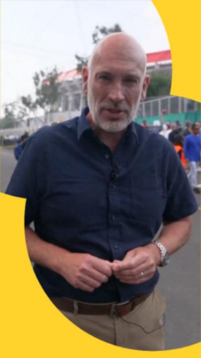 BBC Sports Editor Dan Roan stood in front of a stadium. He's wearing a navy shirt and beige trousers.
