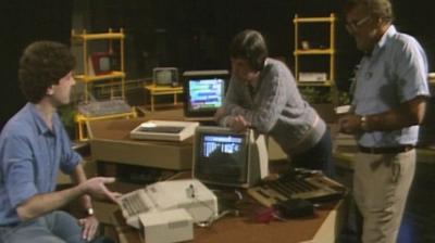 Three men, including John Craven and Ian McNaught-Davis, stand around a desk with a computer