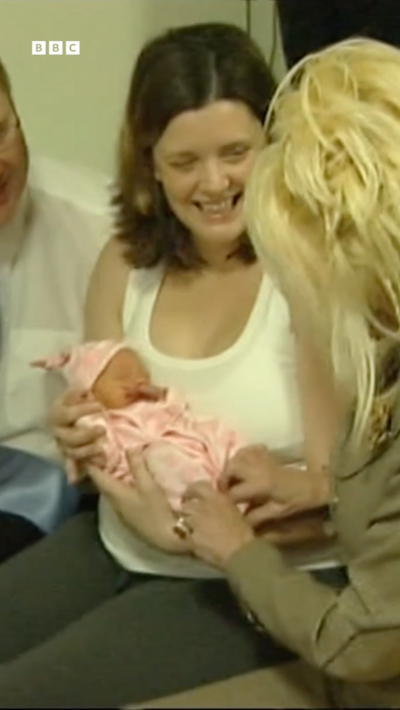 Dolly Parton holds a tiny baby in pink clothes while the baby's parents look on