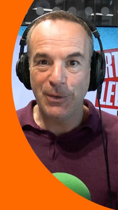 Martin Lewis is sat in front of a green mic with black headphones on. He is mid speech.