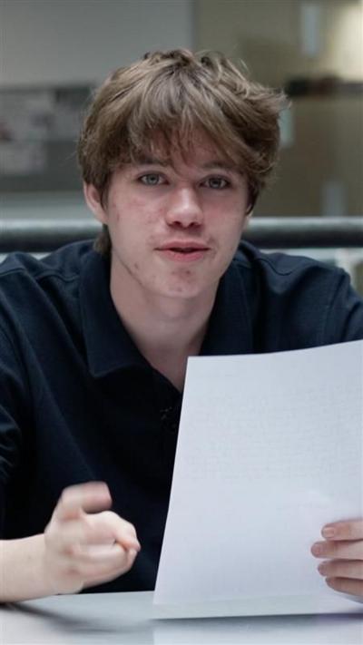 Boy holds letter in his hand. He's wearing a black t-shirt and has brown hair