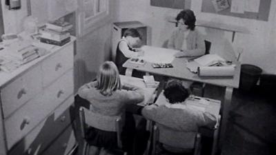 Teacher sits at a desk with three children