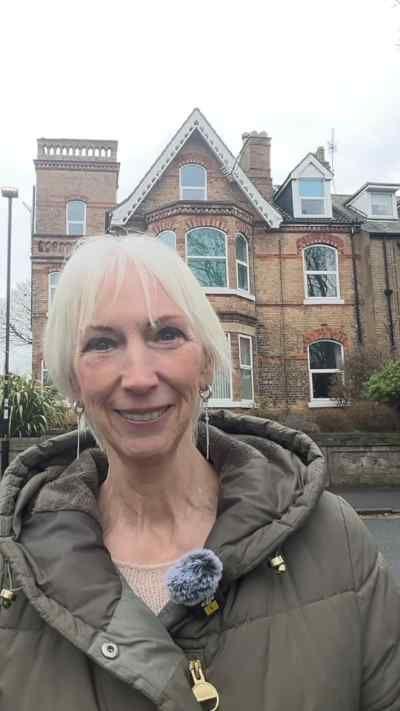 Sue Taylor outside her home in Hornsea. She has white hair and is wearing a large green coat.