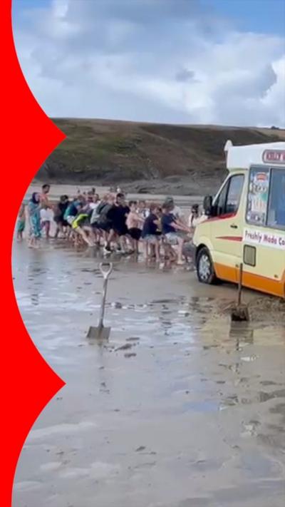 A group of people pulling an ice cream van out of the sand.