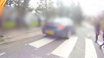 A car is passing over a zebra crossing. It is blurred, and the people around the car are also blurred or out of focus.