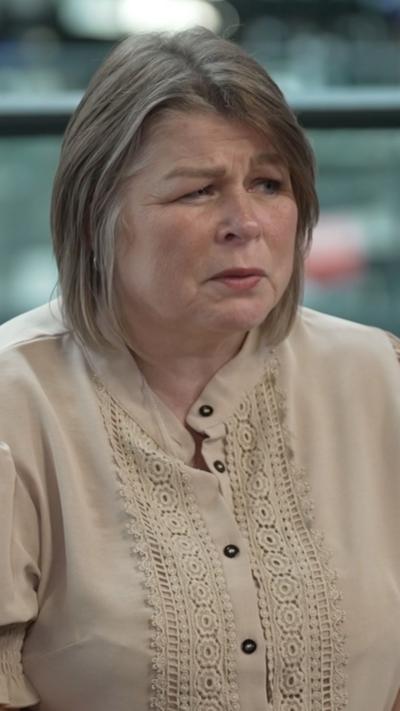 Woman with short brown hair with highlights wearing light beige blouse.