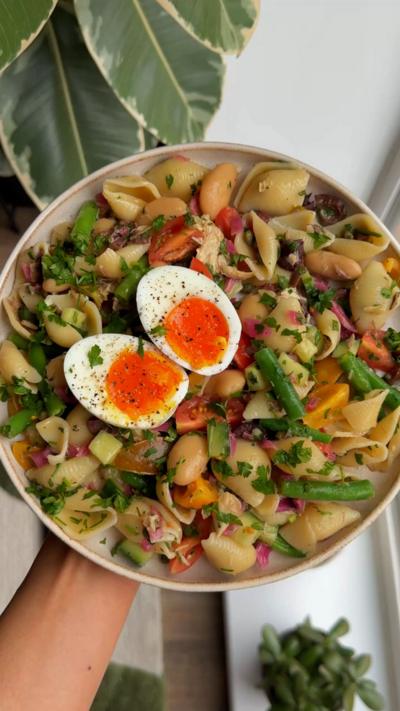A bowl full of pasta and green with sliced boiled egg on top