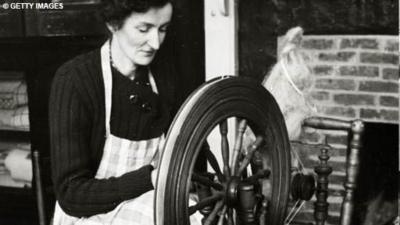 A woman sits at a spinning wheel