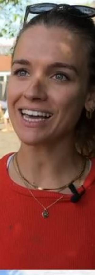 A woman in a red top smiling, she has dark hair pulled back with sunglasses on her head. 