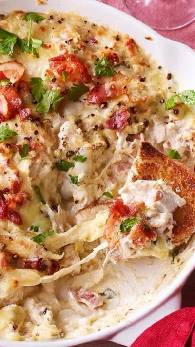 Dish of creamy melted cheese sauce with bacon on the top, and a small piece of crusty bread on the side.