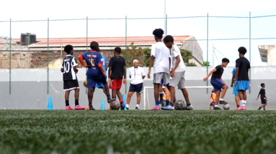 Children play football on an artificial pitch in Cape Verde while a coach oversees their progress