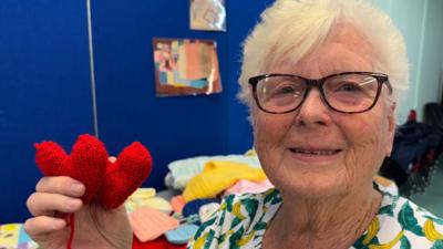 Marilyn Wyatt holding up a pair of knitted hearts