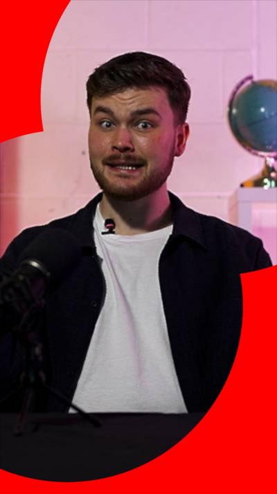 Conor has short brown hair and wears a black shirt over a white T-shirt. There is a globe in the background