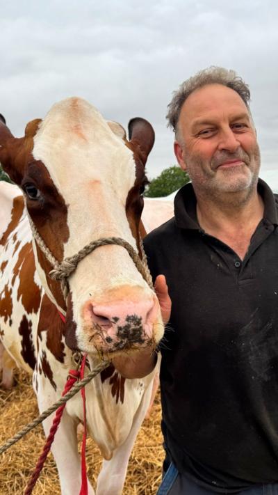 Man wearing a black polo top standing next to a cow at an agricultural show