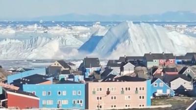 Iceberg collapsing creating wave near city with colourful houses