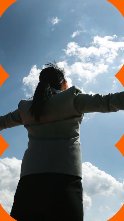 A suited woman with her arms stretched open. She is looking up into the sky