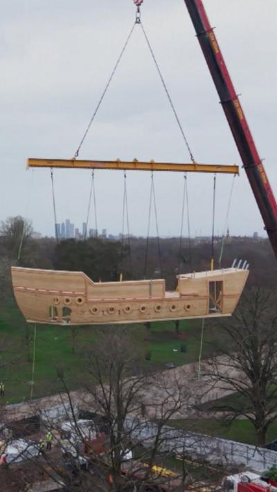A wooden ship is lifted into position in Kensington Gardens.