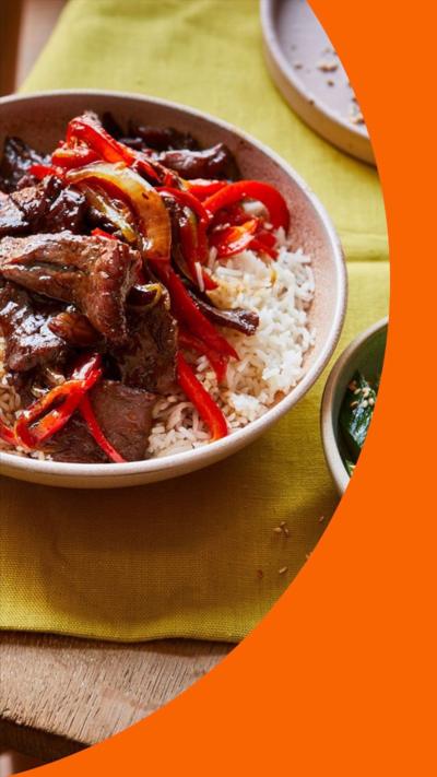 A bowl of cooked beef and peppers in a dark sauce with rice 