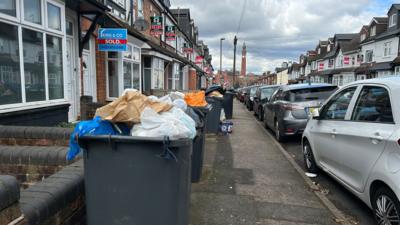 Several black wheelie bins overflowing with rubbish on a Birmingham street