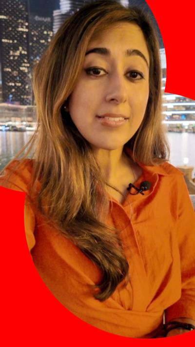 Azadeh Moshiri in an orange top standing near a body of water