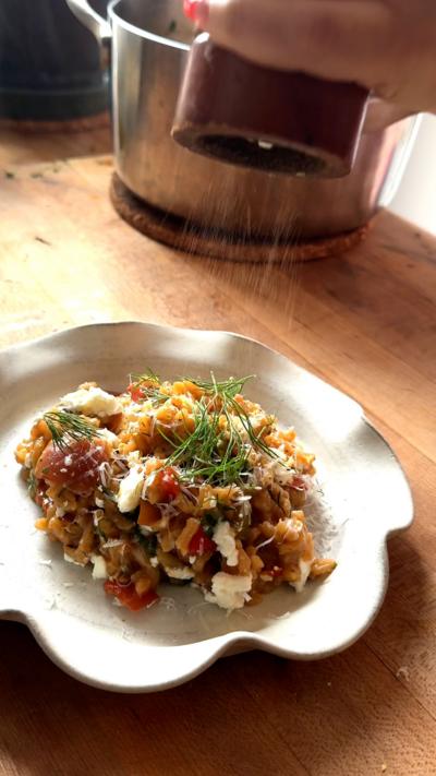 A white place with crimped edges holds a portion of the baked rice. A pepper grinder is being held above it with flecks of pepper falling onto the dish below.